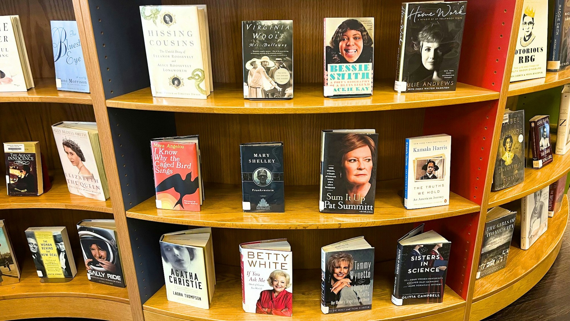 A bookshelf displays various books, including biographies and memoirs of notable women, showcasing diverse authors and figures.