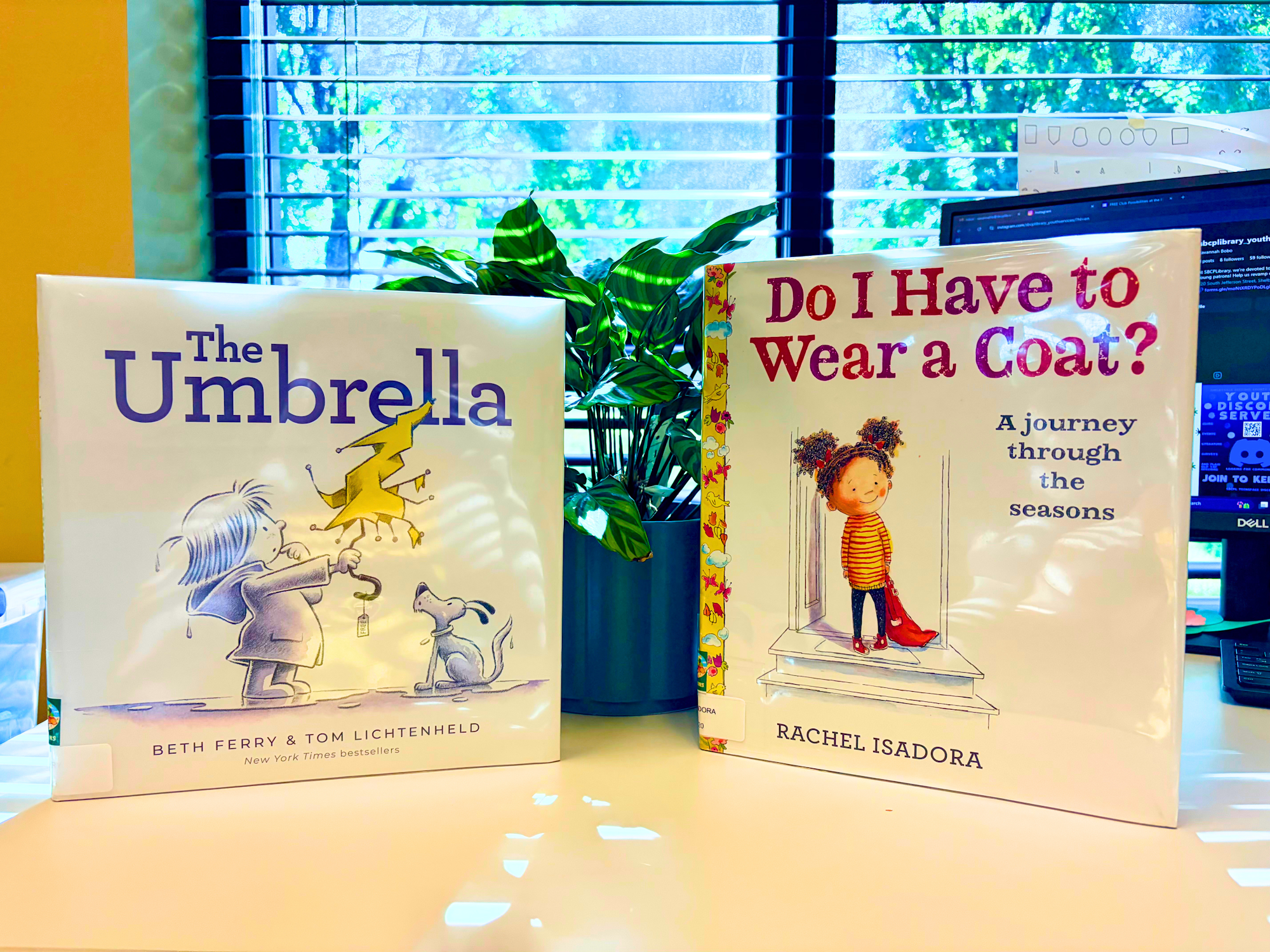 Two children's books on a table: "The Umbrella" by Beth Ferry & Tom Lichtenheld, and "Do I Have to Wear a Coat?" by Rachel Isadora.