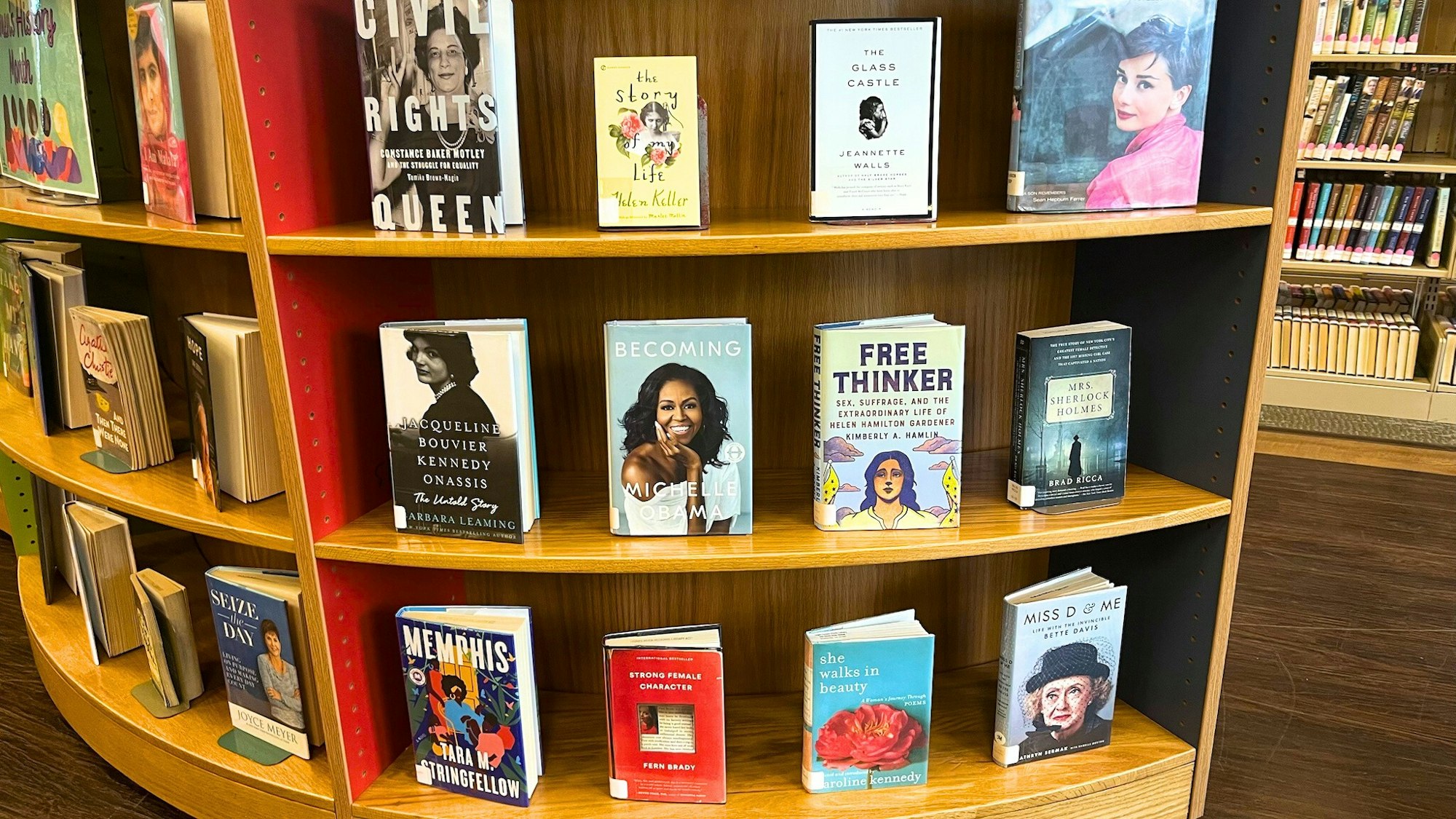 The image features a book display with various titles related to influential women, including memoirs and historical accounts.
