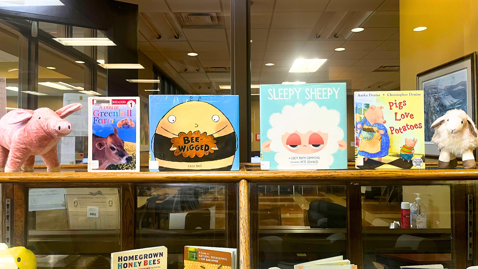The image features storybooks about farm animals and plush toys, including a pig and a sheep, displayed on a shelf.