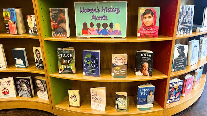 The image features a display for Women's History Month, showcasing various books by and about influential women.