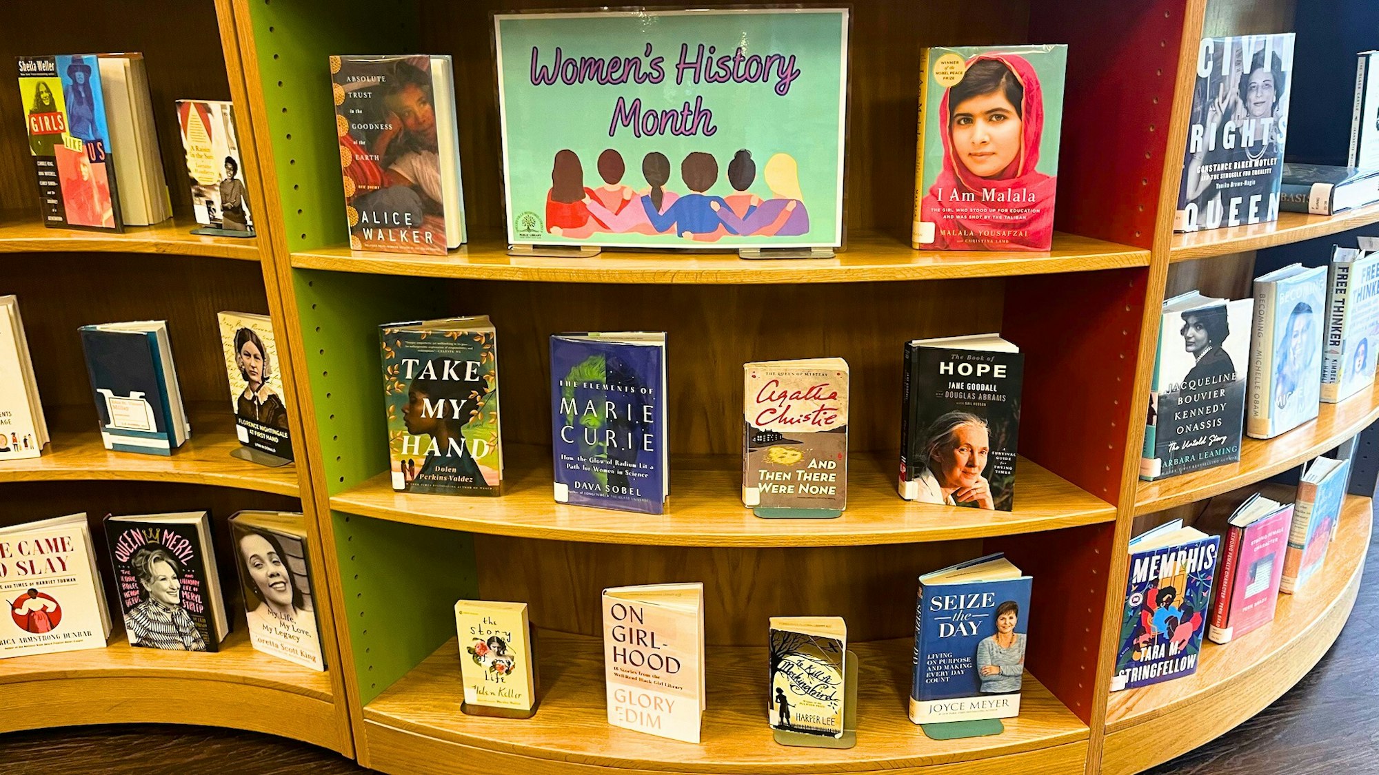 The image features a display for Women's History Month, showcasing various books by and about influential women.