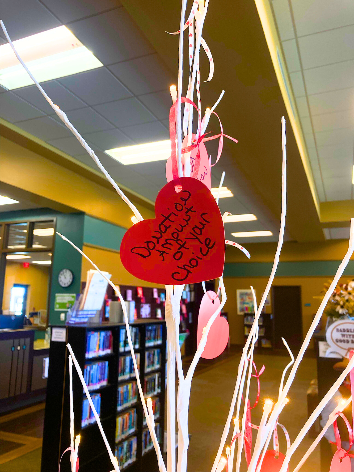 A heart-shaped card on a decorated tree branch reads "Donation of your choice" inside a library.