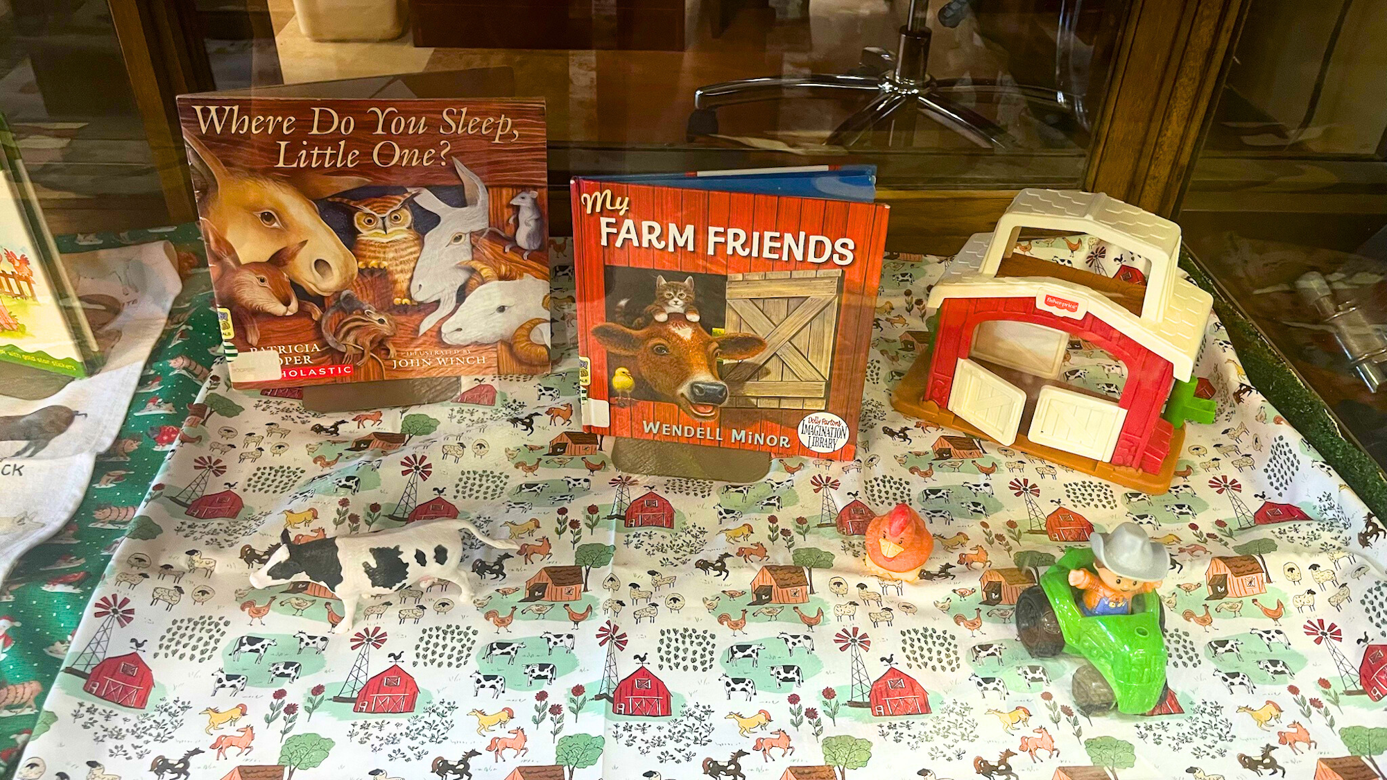 The image features children's books about farm animals, a toy barn, and animal figures, all on a farm-themed tablecloth.