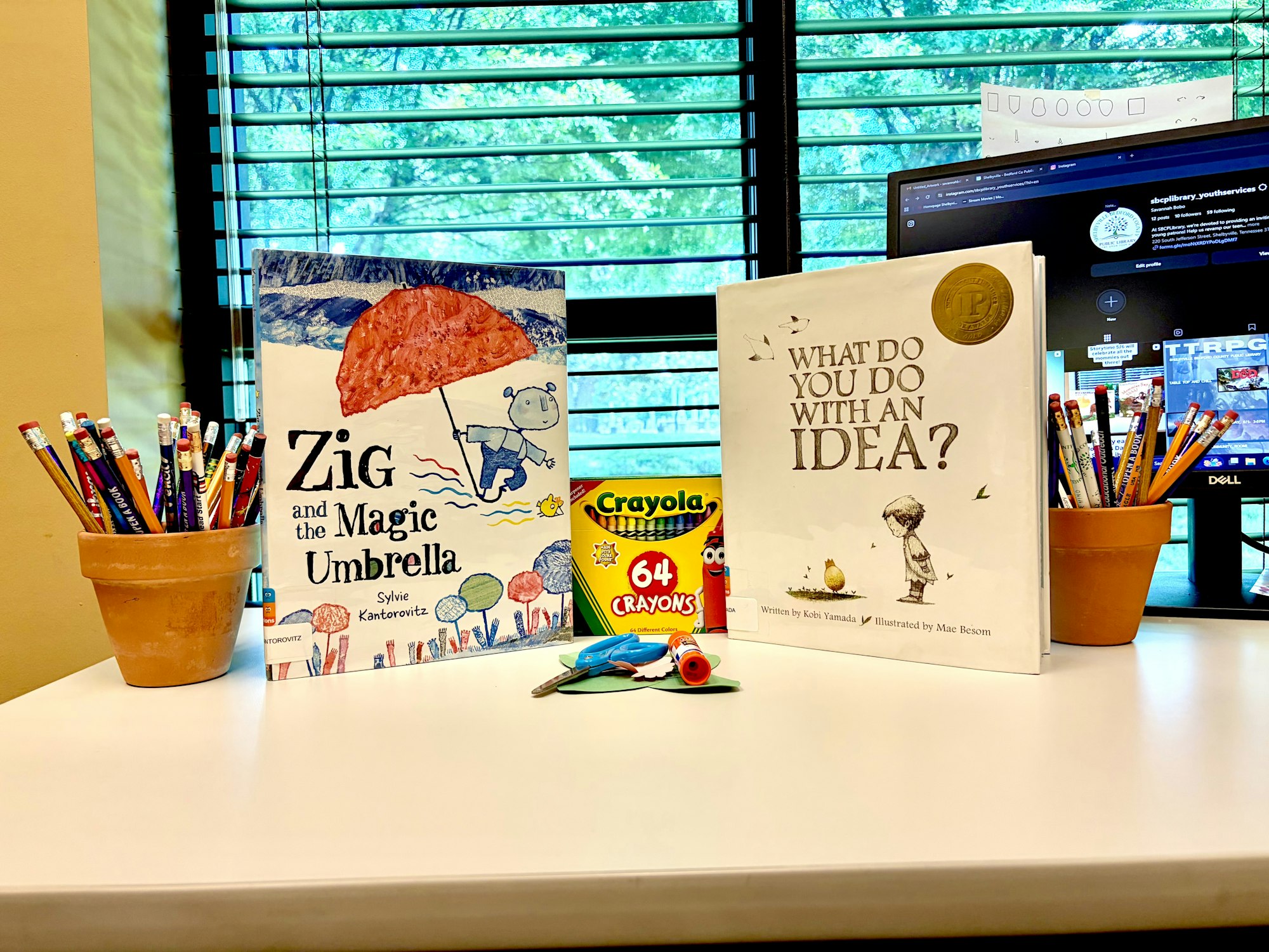 The image features two children's books on a desk, colorful pencils in pots, and a box of 64 Crayola crayons.