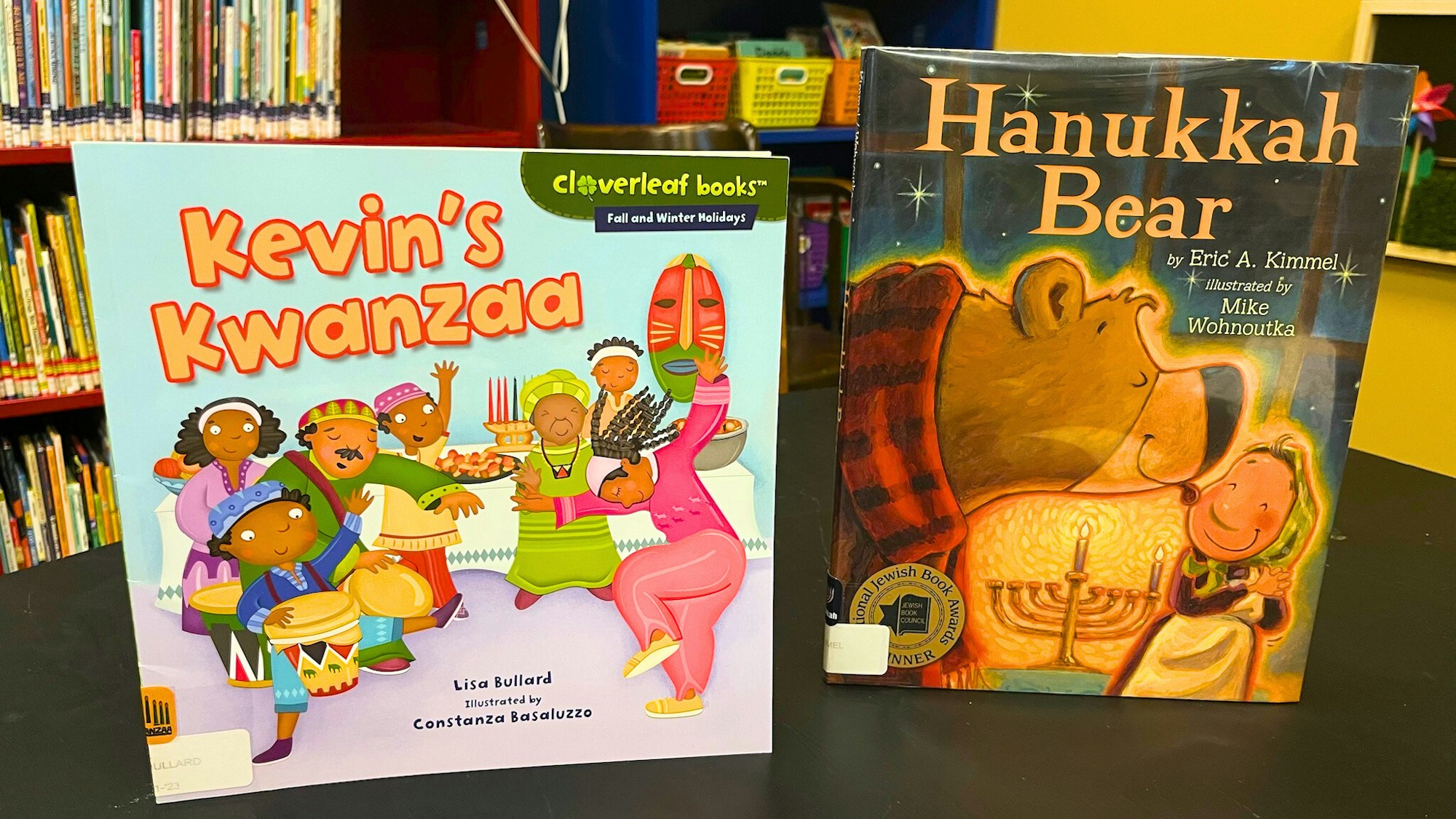 The image shows two children's books: "Kevin's Kwanzaa" and "Hanukkah Bear," both celebrating cultural holiday themes.