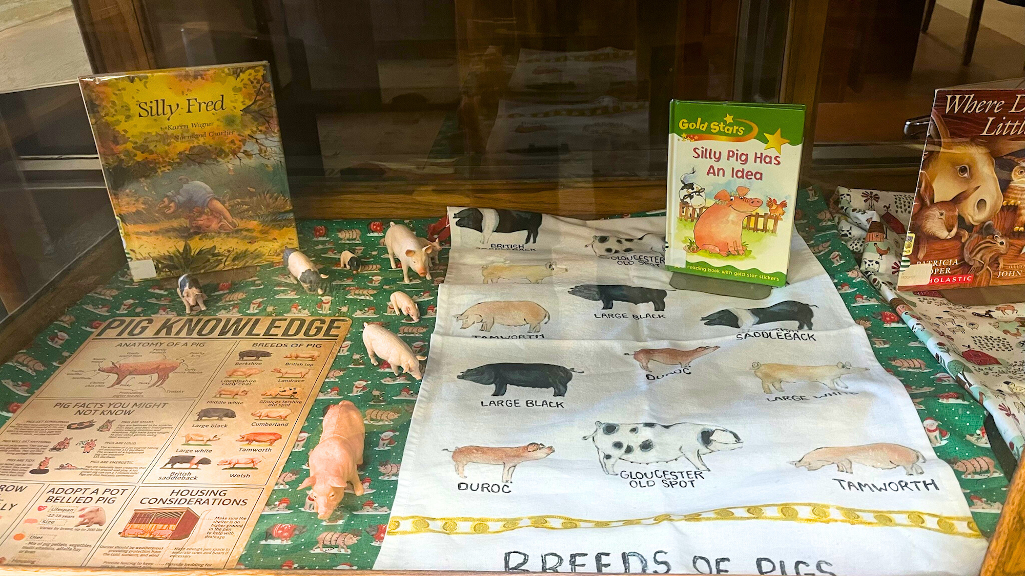 A display featuring pig-themed books, pig figurines, and a fabric showing different pig breeds with educational content.