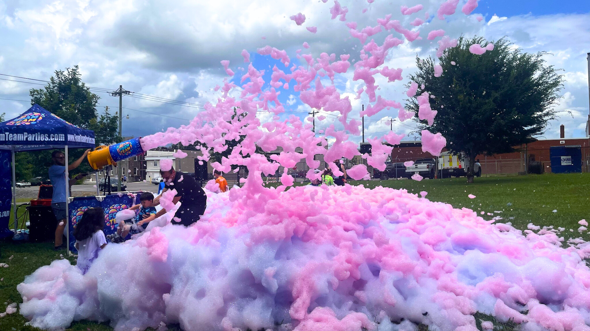 A foam party outdoors with colorful foam being sprayed over people on a grassy area.