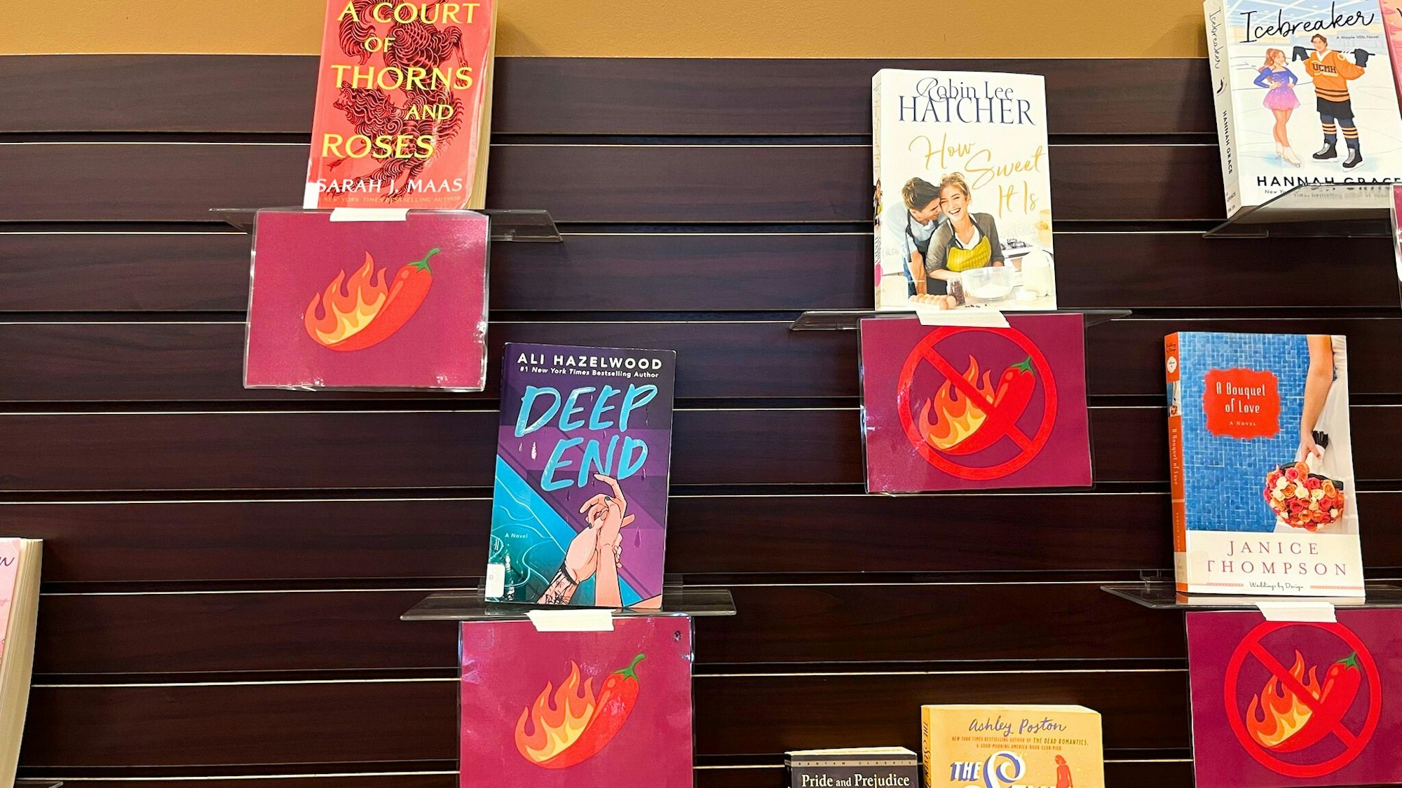 The image shows a book display with romance novels, featuring themed symbols indicating spicy content and those without.