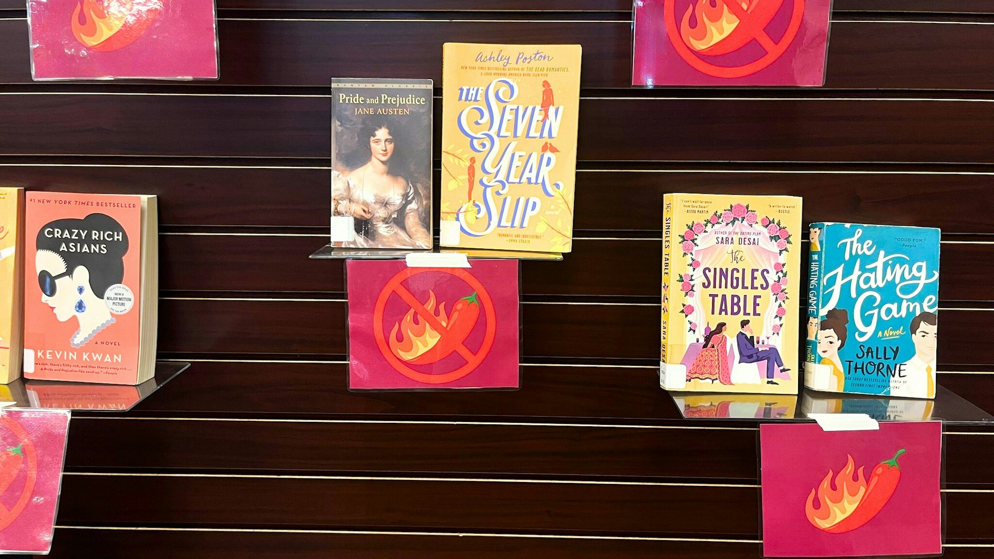 The image shows a display of books including "Pride and Prejudice," "Crazy Rich Asians," and "The Hating Game," with signs.
