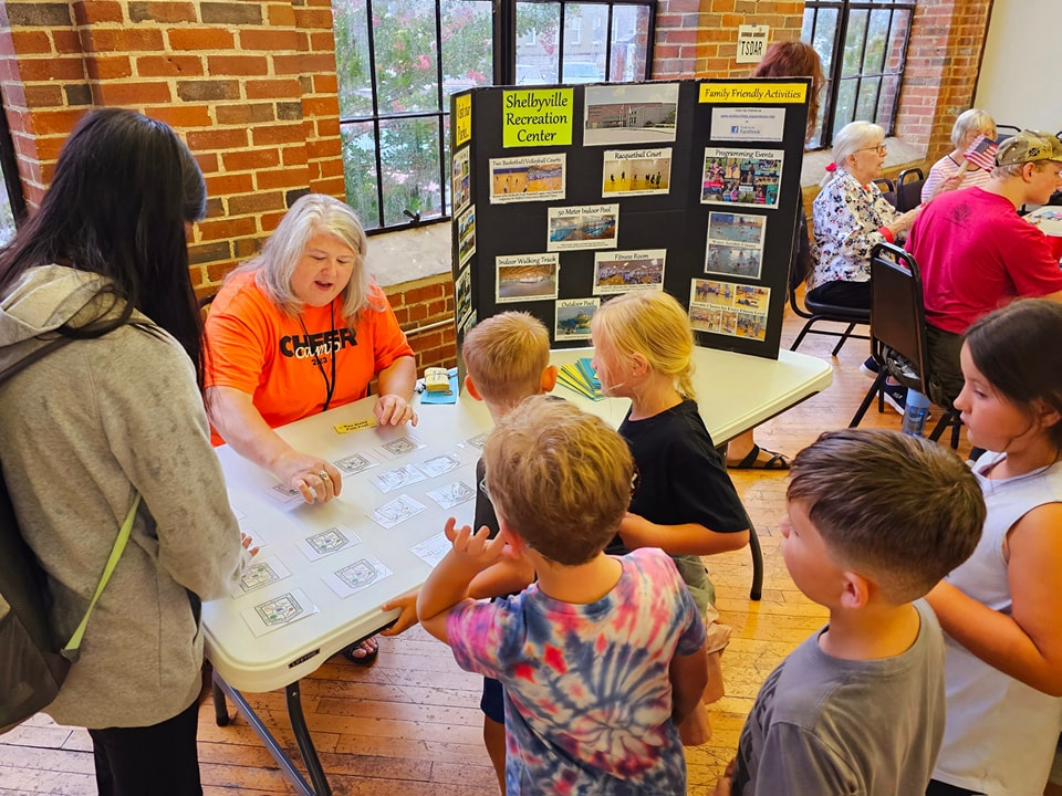 Adults and kids at a table with cards, in a room with informational displays.
