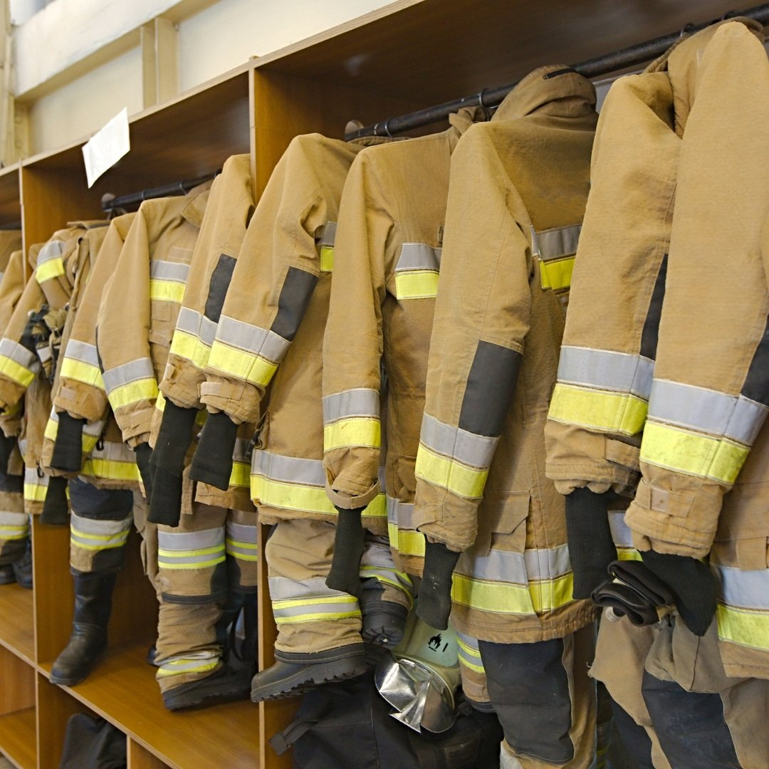 Several firefighter jackets and boots hanging in a row.