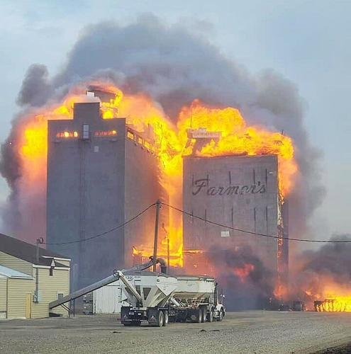 A large building on fire with intense flames and smoke, while a truck stands nearby.