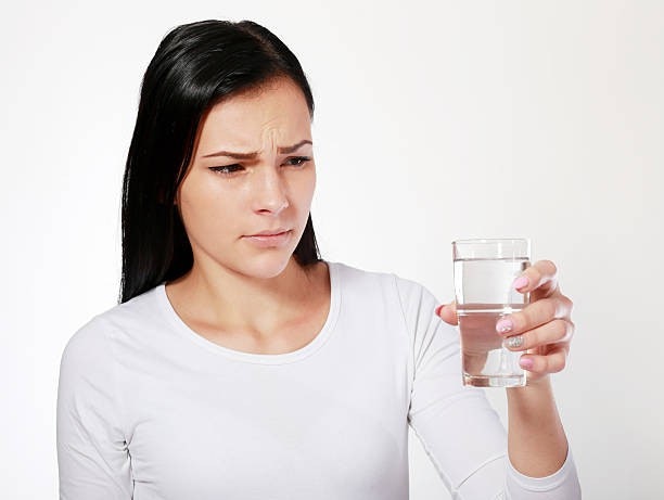 A person in a white shirt looking skeptically at a glass of water.