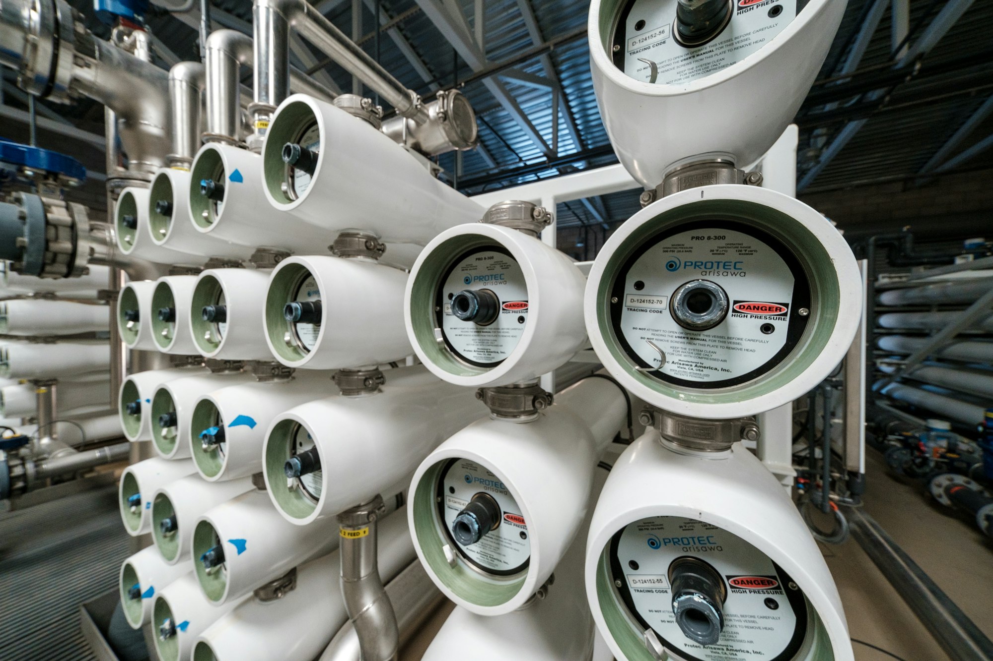 Rows of white cylindrical tanks with “Protec Arisawa” labels, likely part of an industrial filtration system.