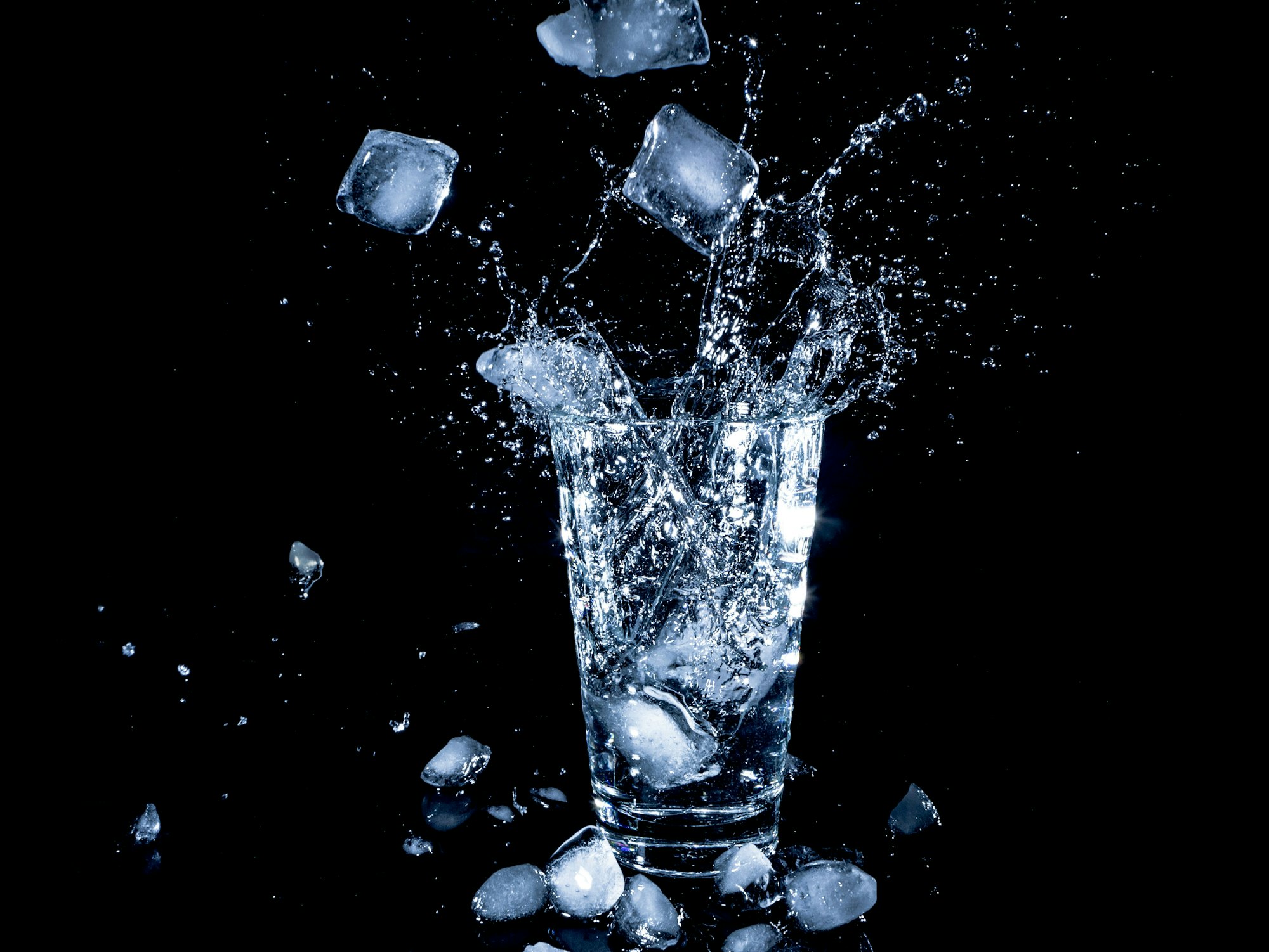 Ice cubes splashing into a glass of water against a black background.
