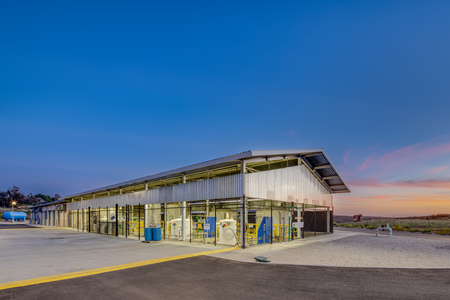 A modern, industrial-style building with glass windows, under a clear sky during sunset.