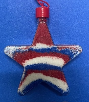 A star-shaped ornament filled with red, white, and blue sand, likely themed for a patriotic celebration.