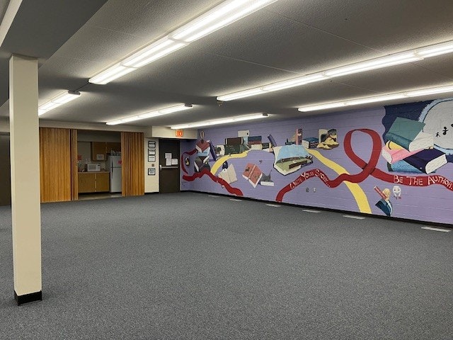 A large, empty room featuring a colorful mural on one wall and overhead fluorescent lights.