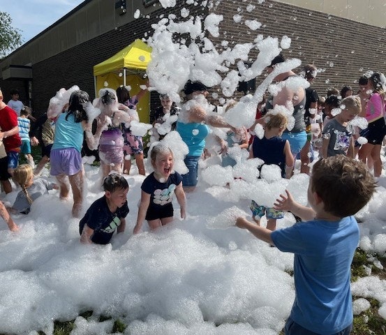 A fun outdoor event with kids playing in bubbles, splashing and laughing amidst a foam-filled area.