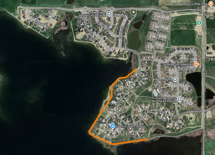 A satellite view of a residential area with marked roads, businesses, and parks, bordered by a body of water on the left.