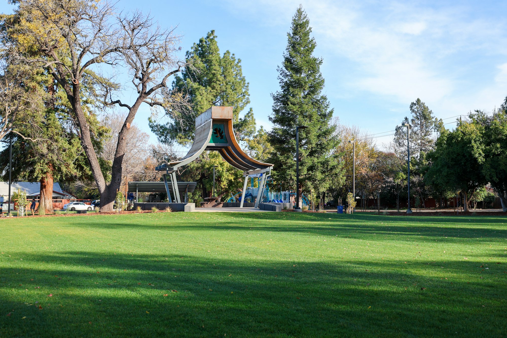 A park with tall trees and a large, unique slide structure on a sunny day.