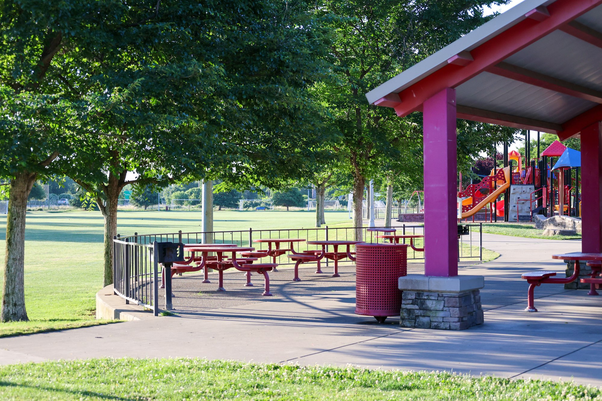 A colorful park with picnic tables, a shelter, and a playground in a grassy area with trees.