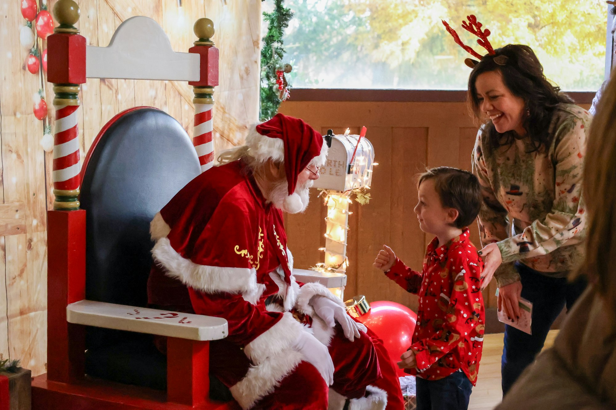 Child meeting Santa, with woman smiling nearby, festive setting.