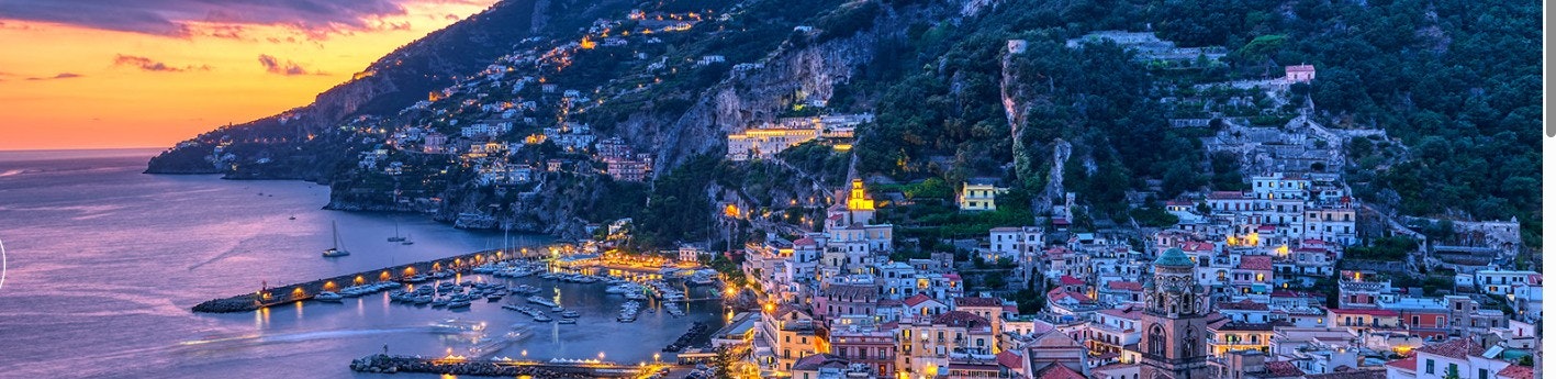A scenic coastal town at dusk, featuring colorful buildings, a marina, and illuminated cliffs along the shoreline.