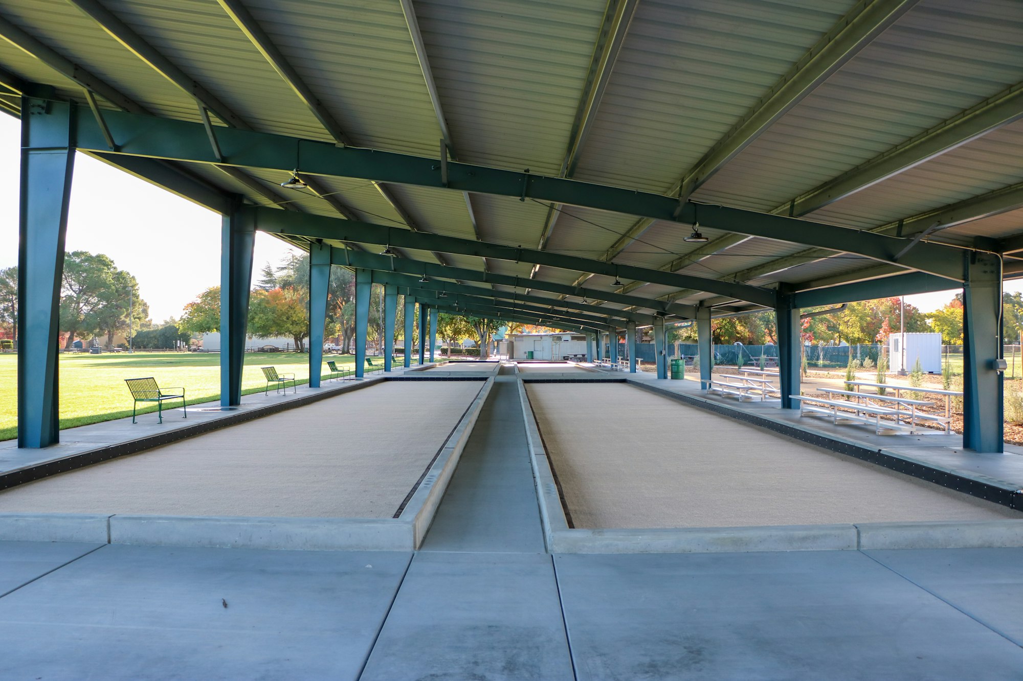 A covered outdoor bocce ball court with benches in a park.