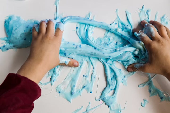 Hands playing with blue slime on a flat surface.