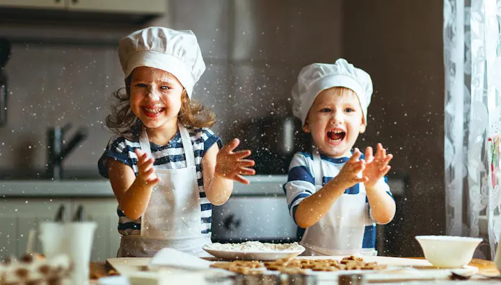 Two cheerful children in chef hats are having fun in a kitchen, playing with flour while baking. Joyful and messy moments!
