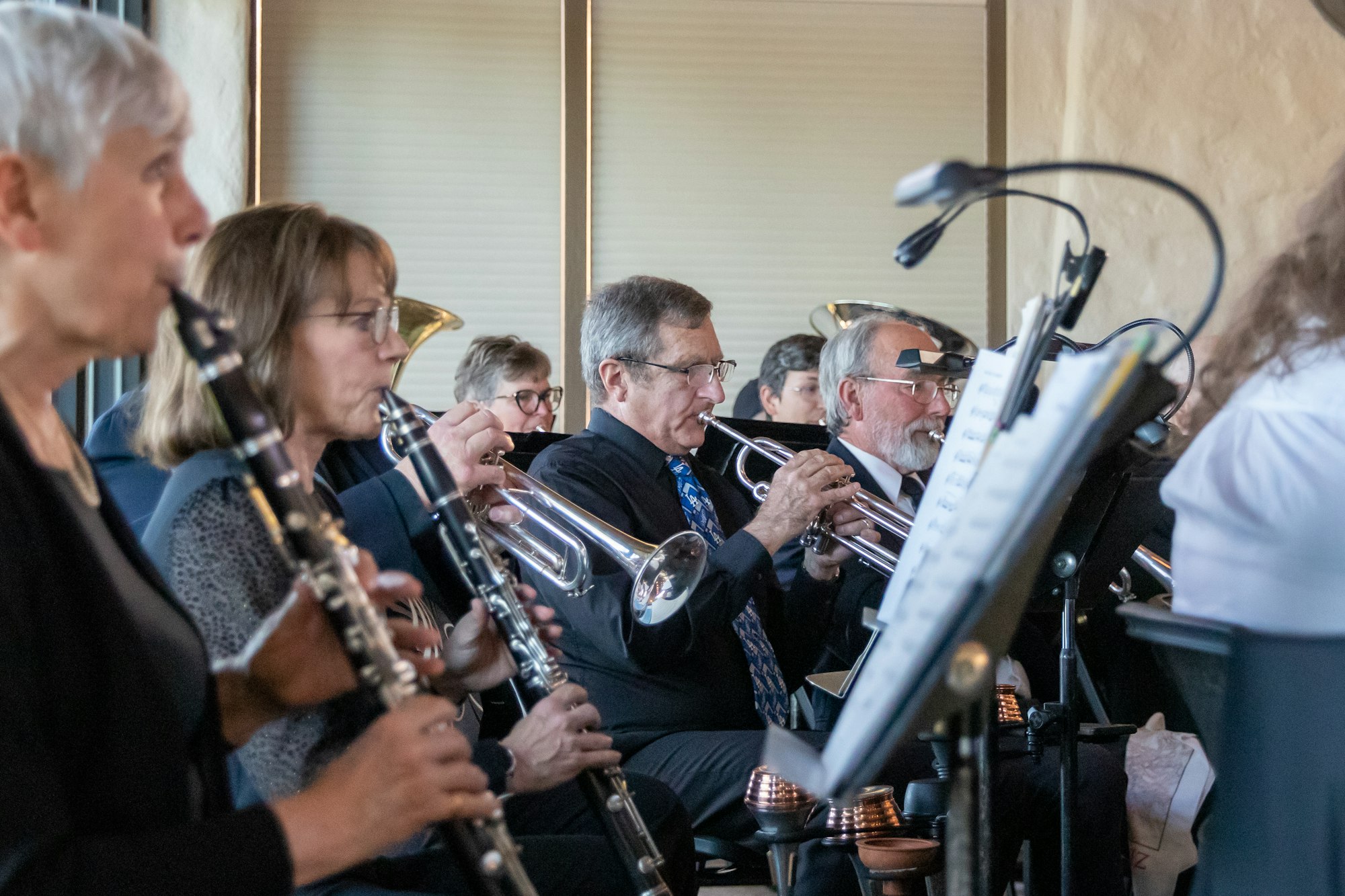 A group of musicians playing brass and woodwind instruments, focused on sheet music on stands.