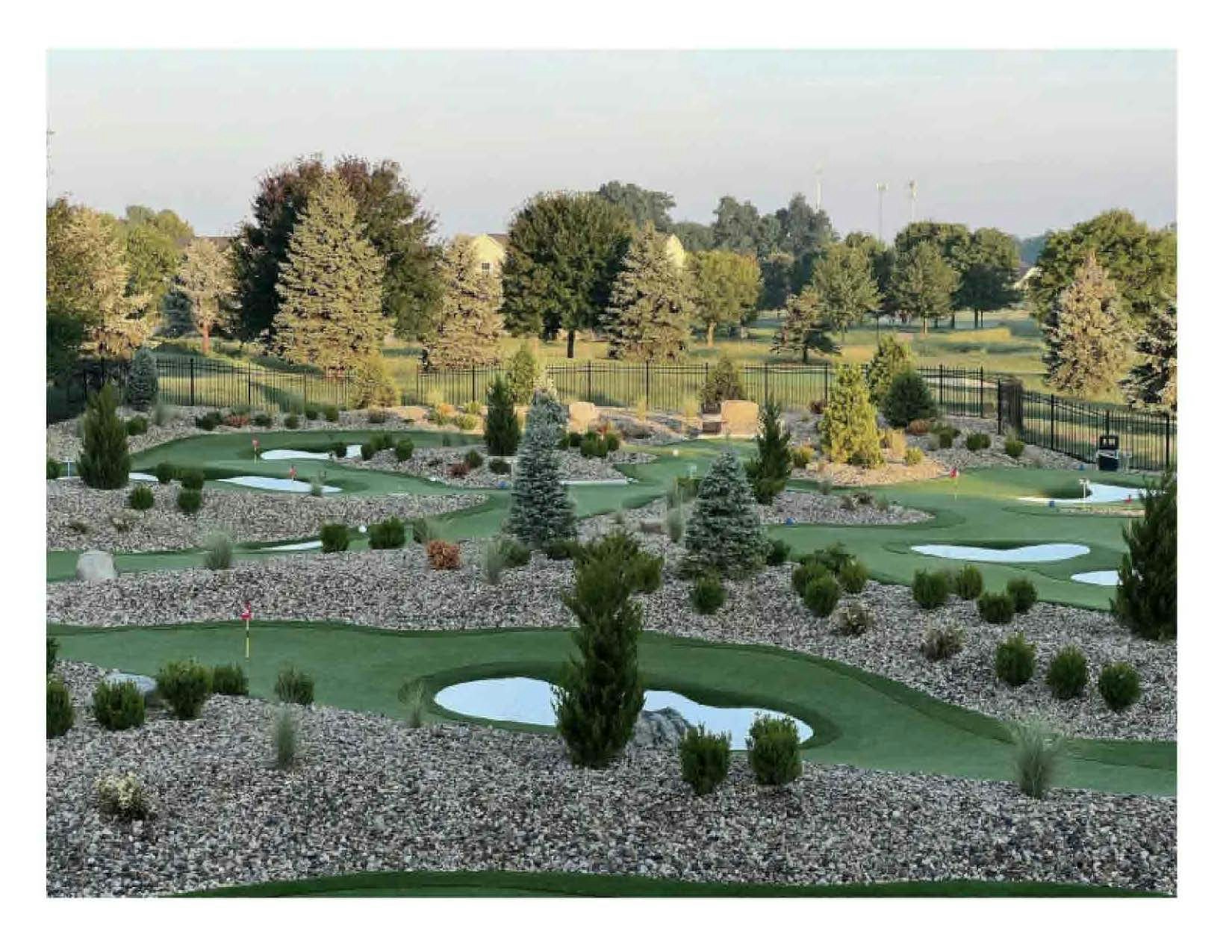 A minigolf course with green tracks, obstacles, stones, and greenery at dusk.