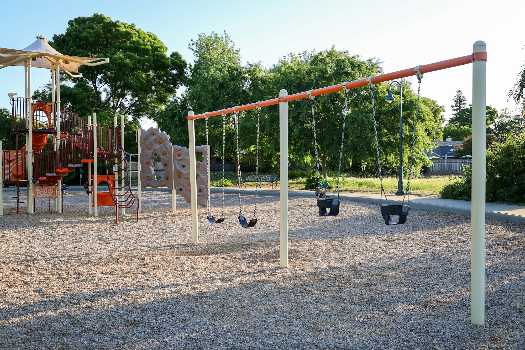 A playground with swings, climbing structures, and slides, surrounded by trees.