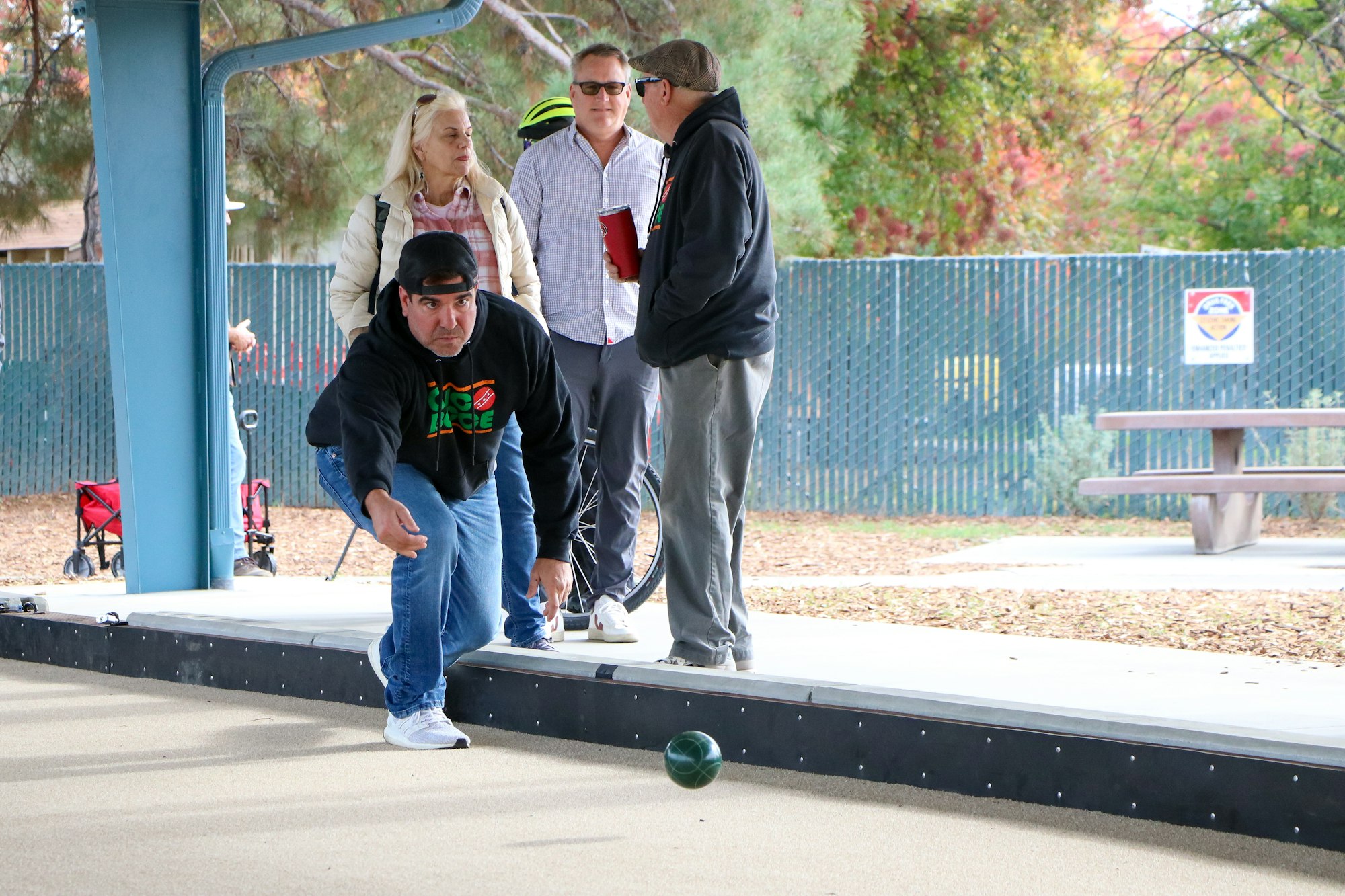 A person bowls on a bocce ball court while others watch.