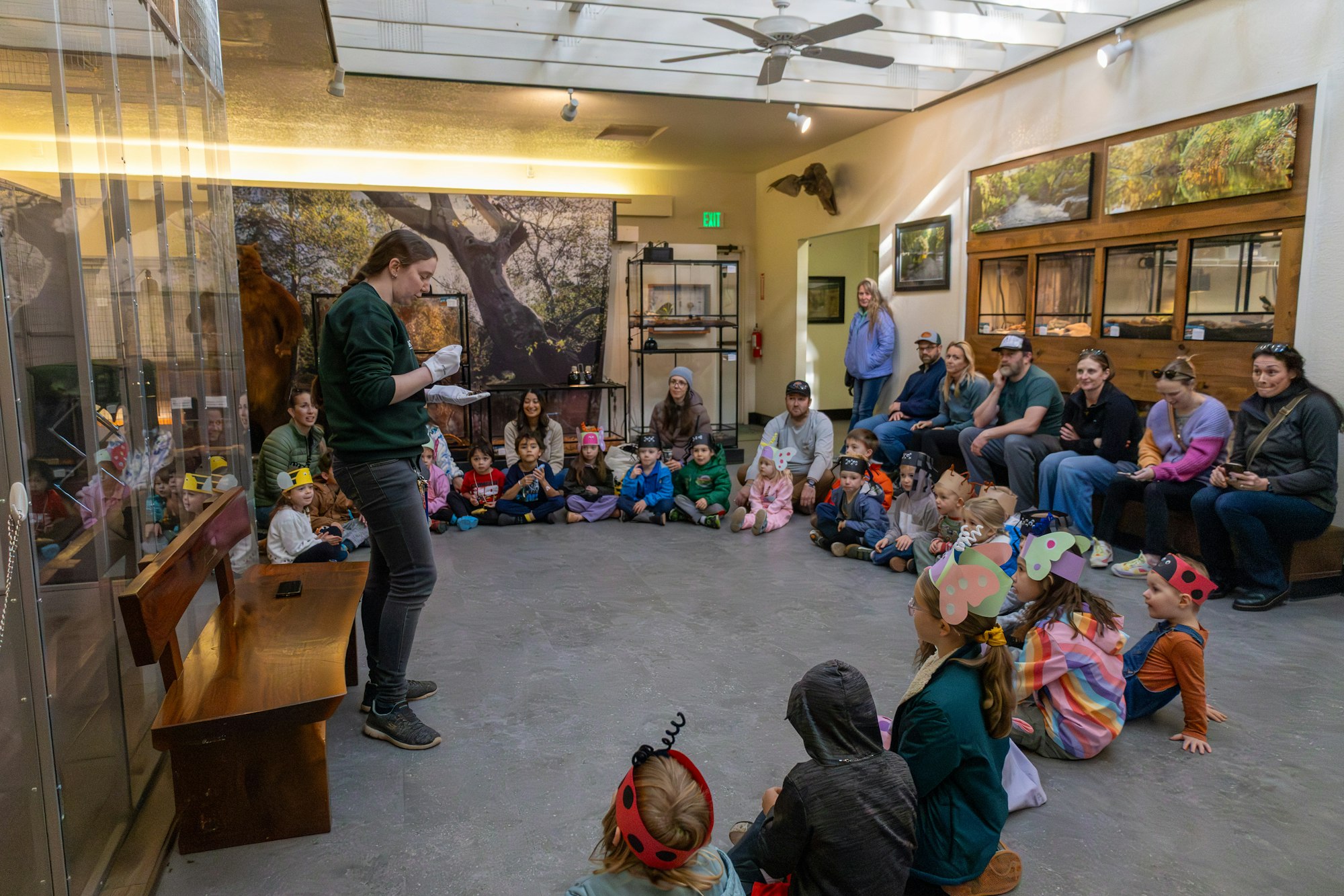 A group of children and adults are gathered for an educational session in a room, with a presenter engaging the audience.