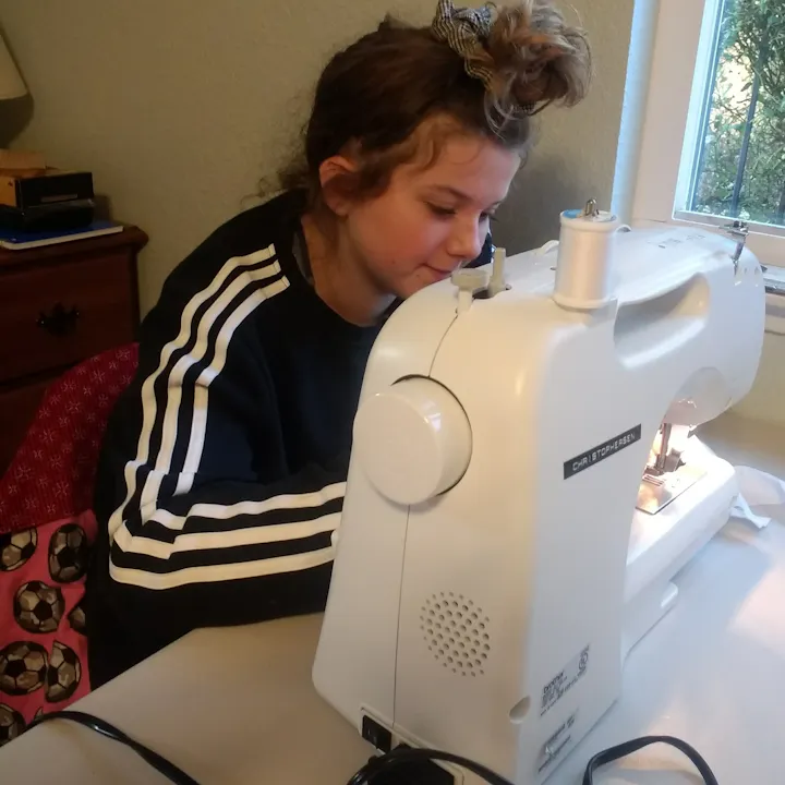 A person is focused on using a sewing machine at a table, working on a sewing project in a cozy indoor setting.