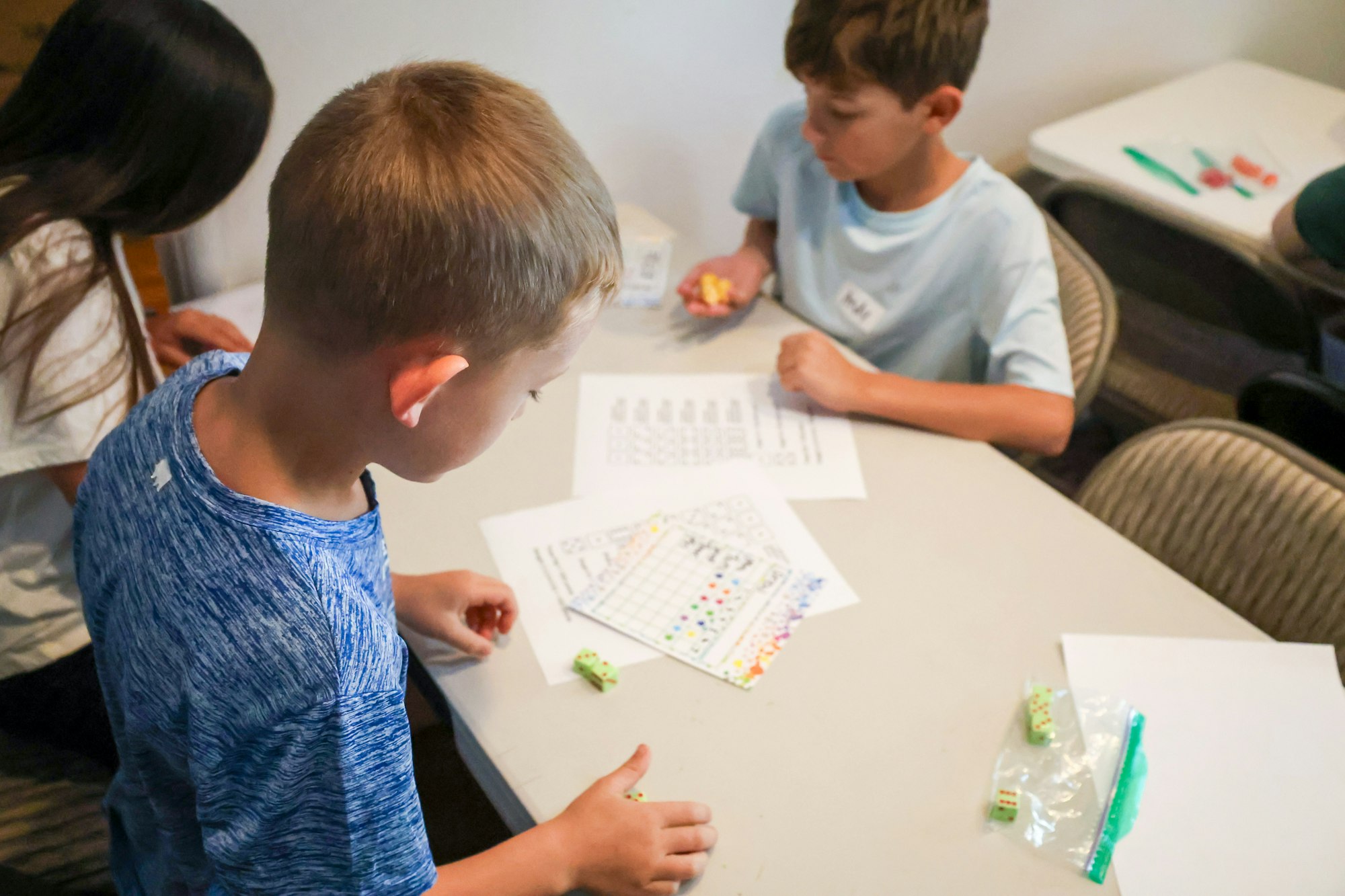 Children playing a dice game with colorful charts on a table.
