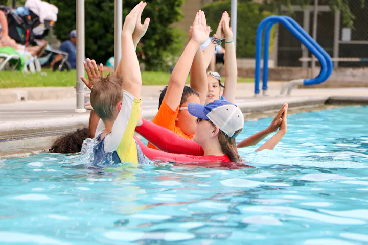 Swim instructor and kids in a pool, raising hands in a group exercise.