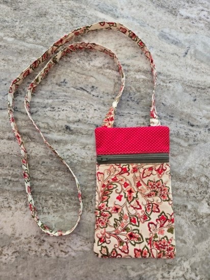 A floral and polka dot fabric pouch with a long strap, resting on a marble surface.