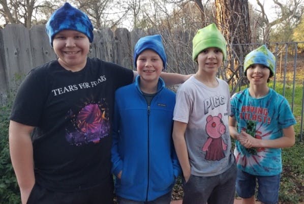 Four smiling people stand outdoors wearing colorful hats, a "Tears for Fears" t-shirt, and a Peppa Pig t-shirt.