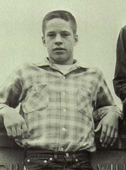 A young person wearing a checkered shirt, with hands in pockets, standing in a confident pose.