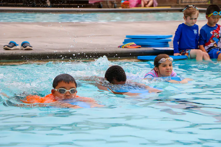 Children are practicing swimming with kickboards in a pool.