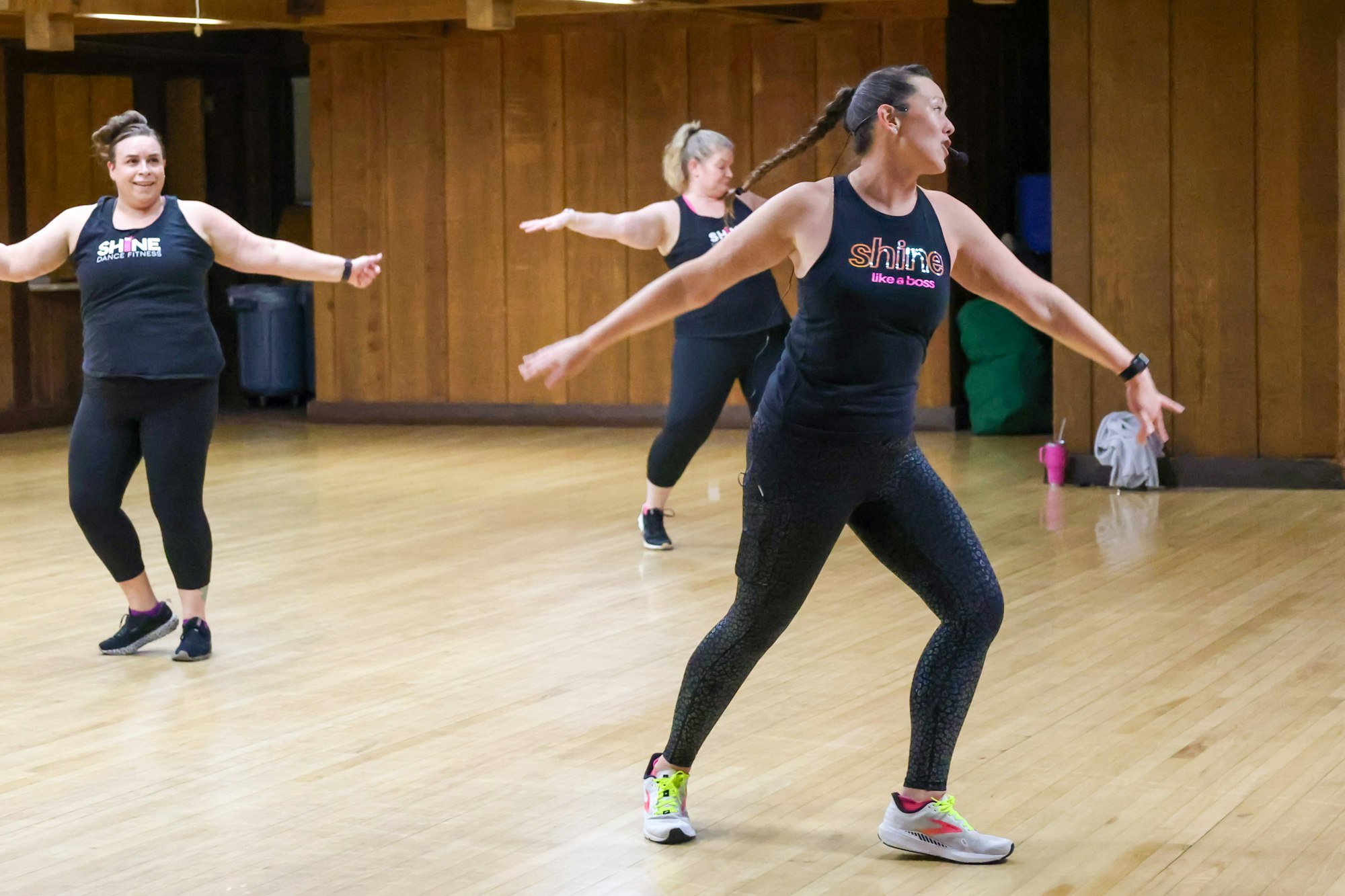 Three women in workout clothes dancing in a wooden-floored room.