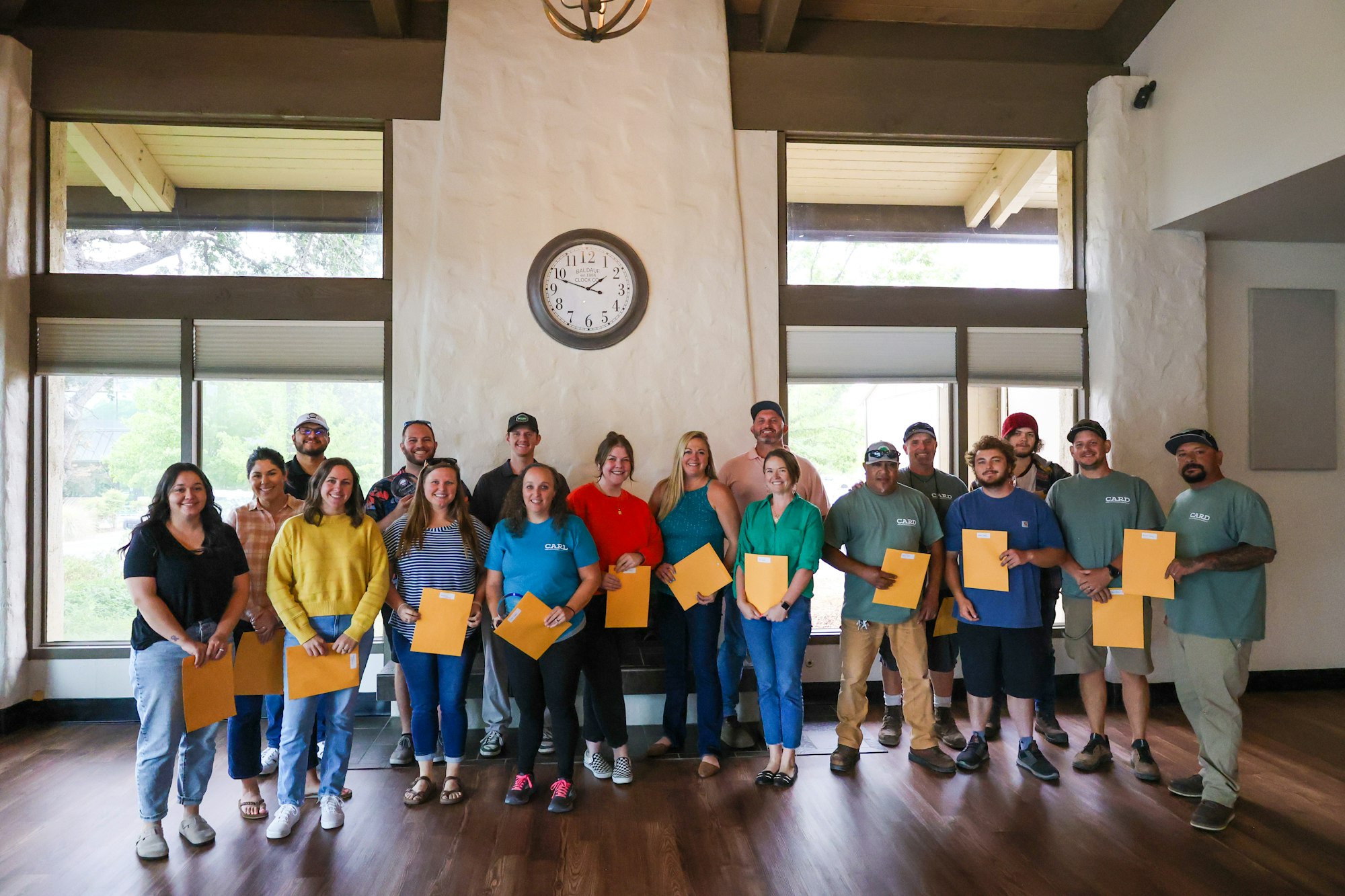 A group of happy people holding certificates inside a room with a large clock on the wall.