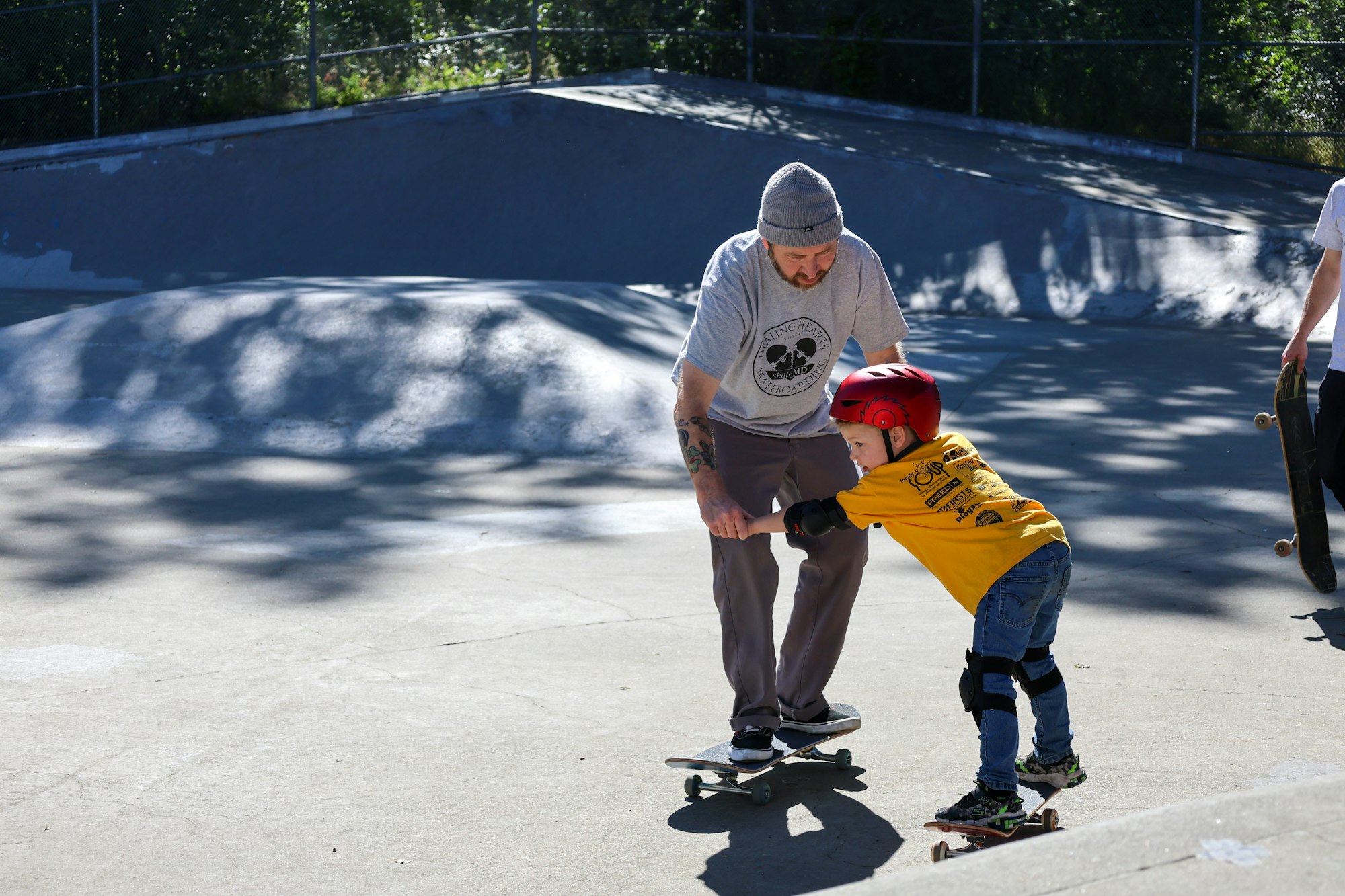 An adult teaching a child to skateboard in a skate park.