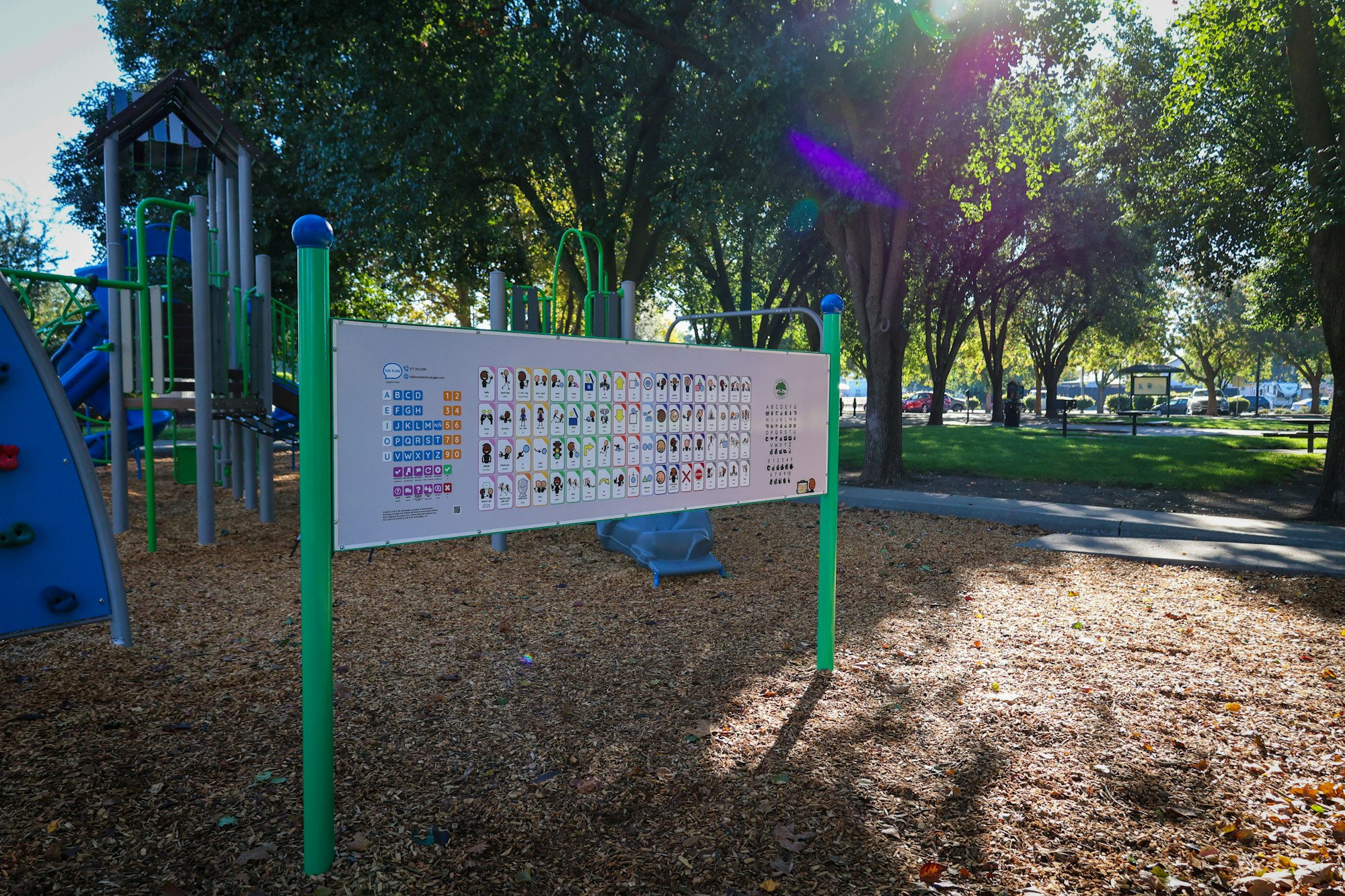 Playground with informational sign, surrounded by trees and woodchip ground.