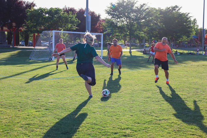 People playing soccer in a park with a goalpost in the background.
