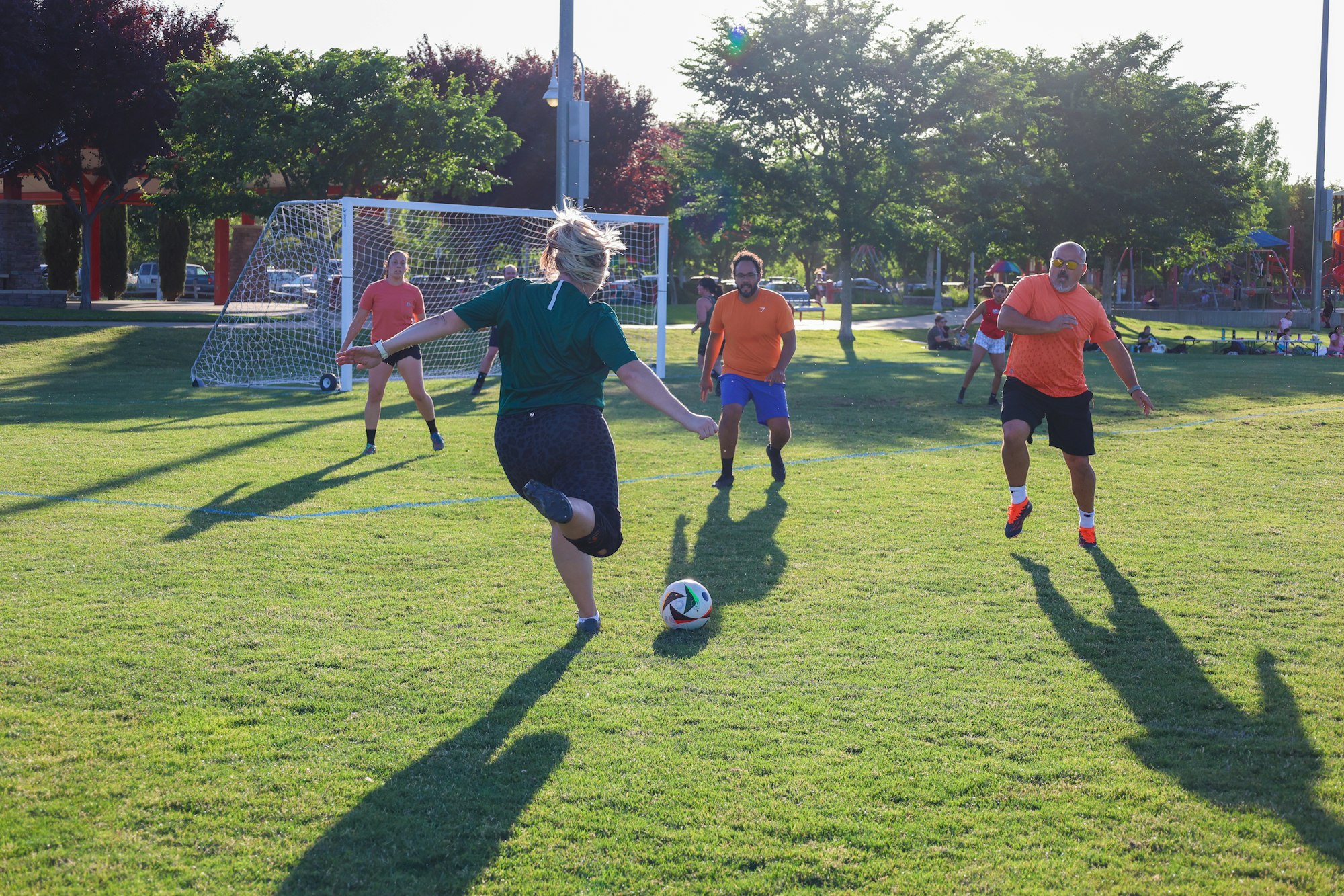 People playing soccer in a park with a goalpost in the background.